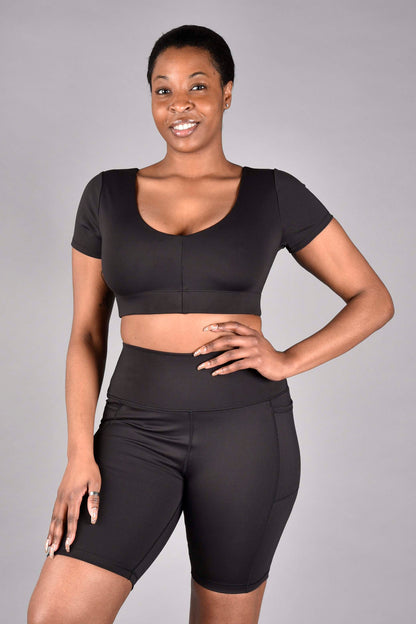 WEAR LOVE MORE Sustainable and Supportive Sports Bras.  Audrey Recycled Core Compression Bra Short Sleeve Longline Bra in Matte Black.  Reversible style.  High neck full coverage and V neck.  Shown with V-neck at front on model wearing Size Medium who is 34DD